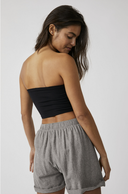 Woman wearing a black strapless top and gray shorts on a plain background