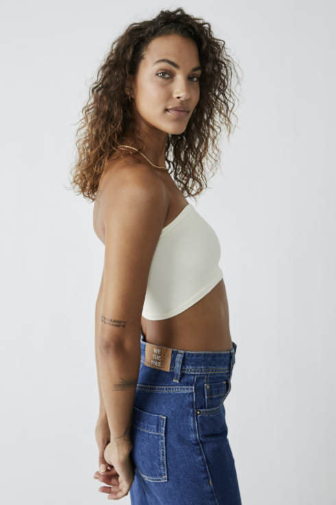 Woman wearing a white strapless top and blue jeans against a plain background