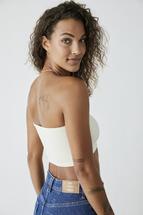 Woman wearing a white strapless top and blue jeans against a plain background