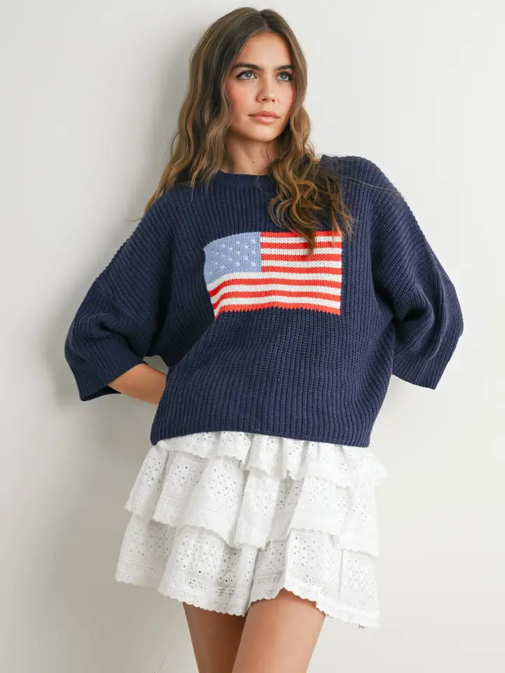 Woman wearing navy sweater with flag design and white skirt on plain background