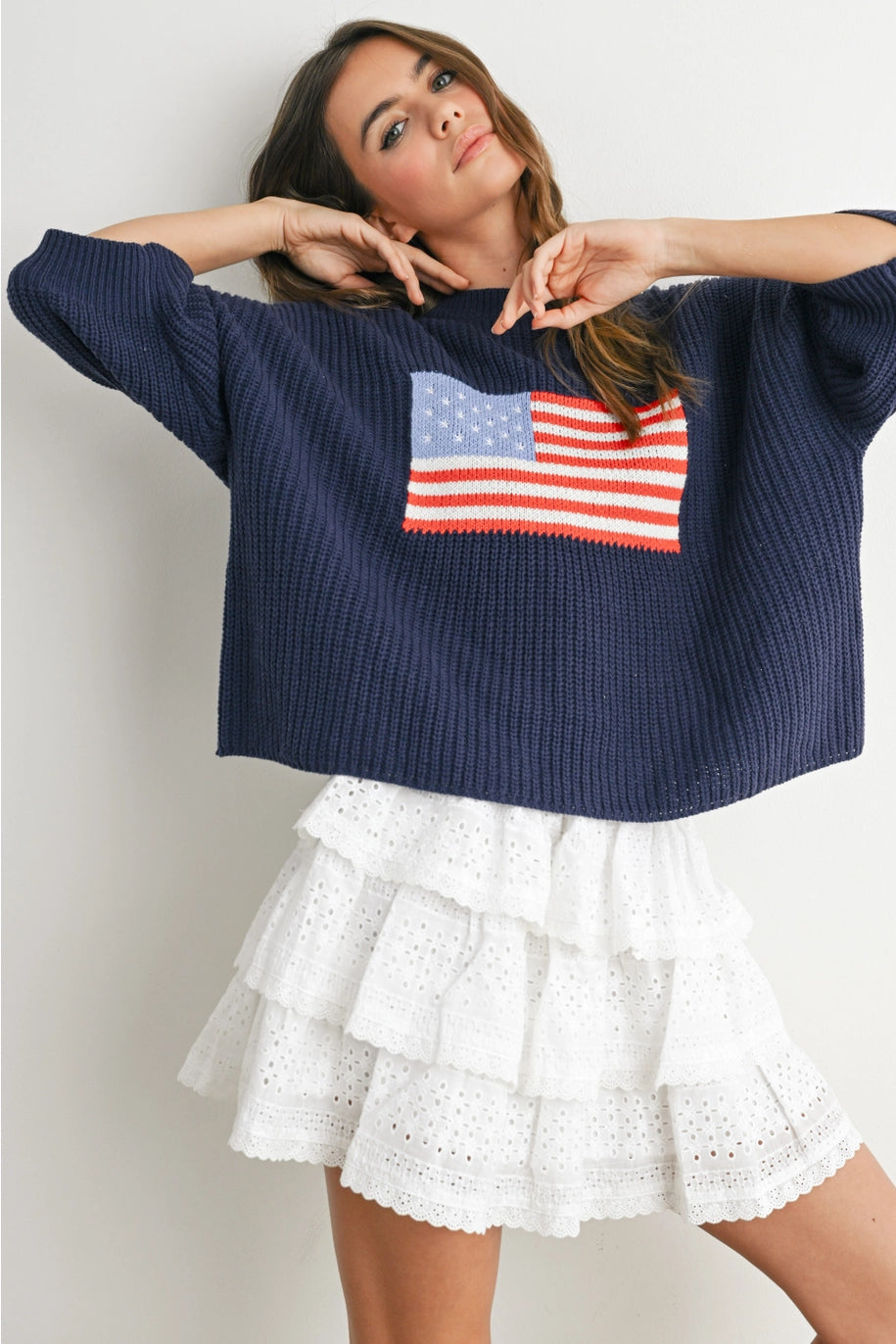 Woman wearing navy sweater with flag design and white skirt on plain background
