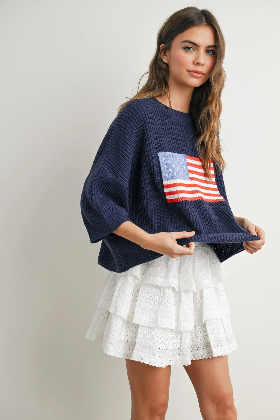 Woman wearing navy sweater with flag design and white skirt and plain background