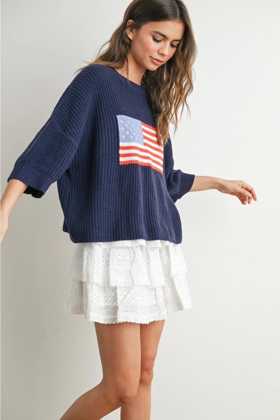 Woman wearing navy sweater with flag design and white skirt on plain background