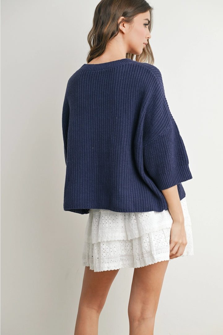 Back of woman wearing navy sweater on plain background