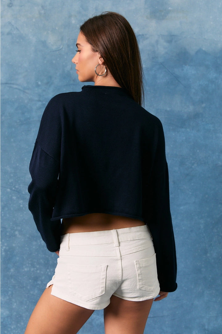 Woman wearing a blue sweater and white shorts against a blue textured background