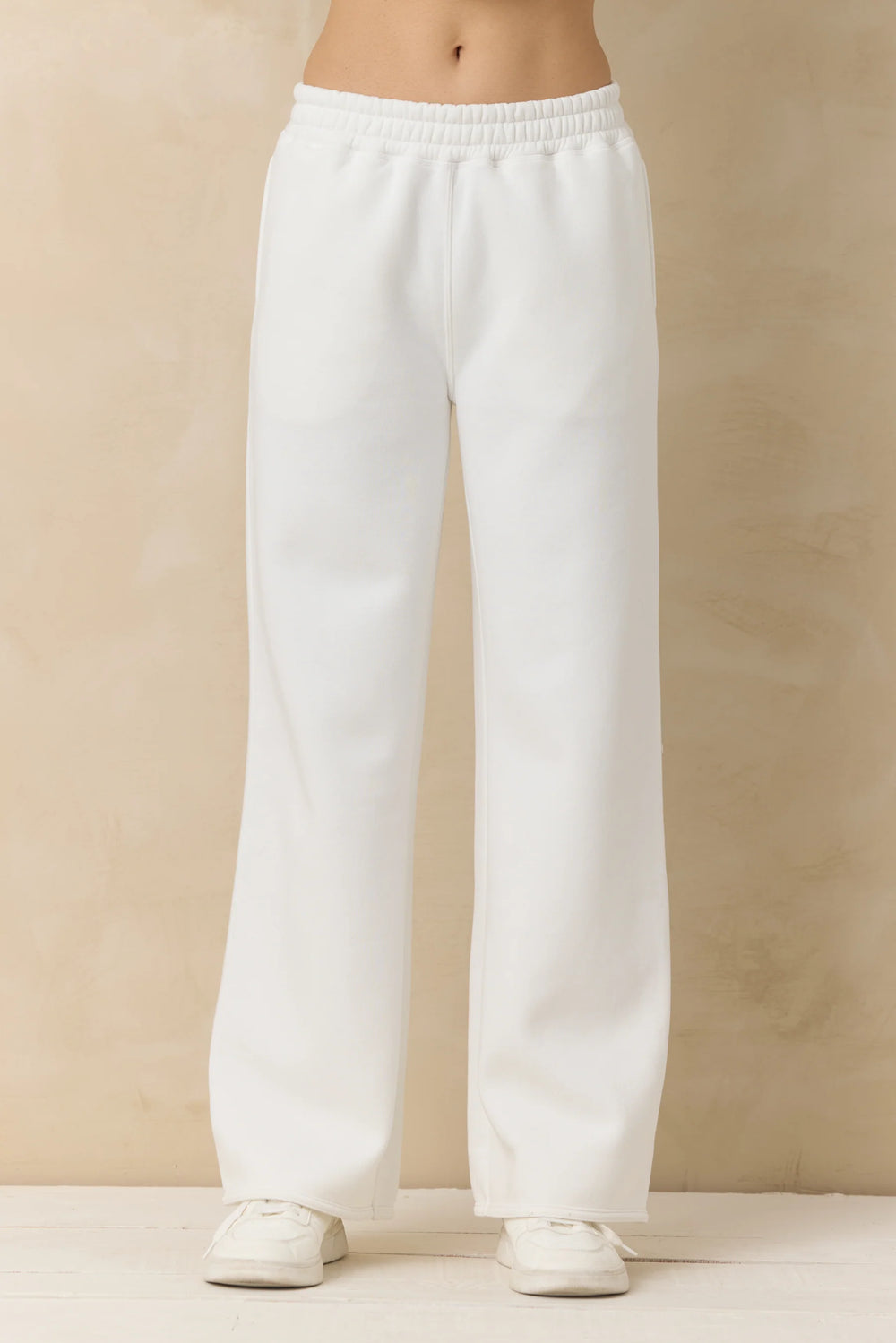 White sweatpants worn by a person on a beige background
