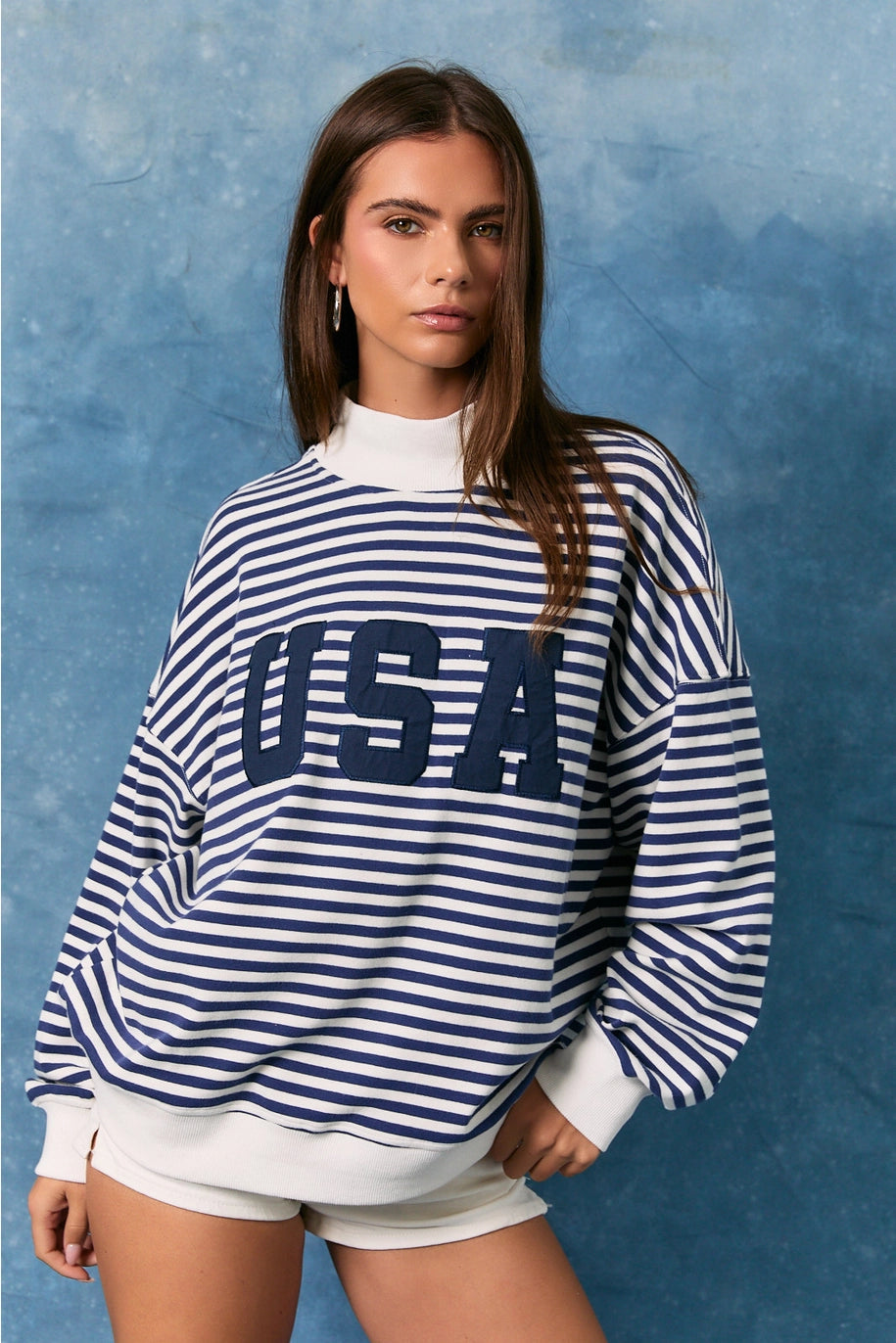 Woman wearing a blue and white striped sweatshirt with 'USA' text against a textured blue background