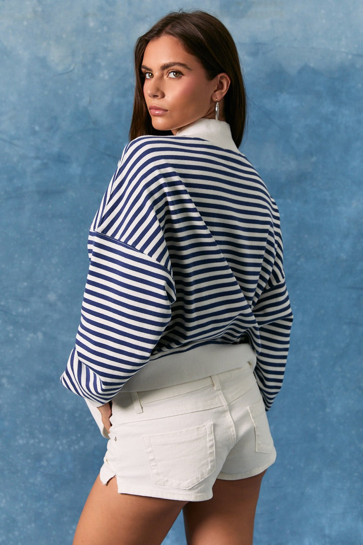 Woman wearing a blue and white striped shirt and white shorts against a blue background