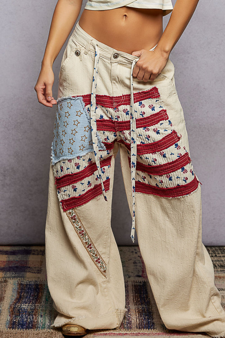 Person wearing a pair of wide-leg pants with patchwork design on a plain background