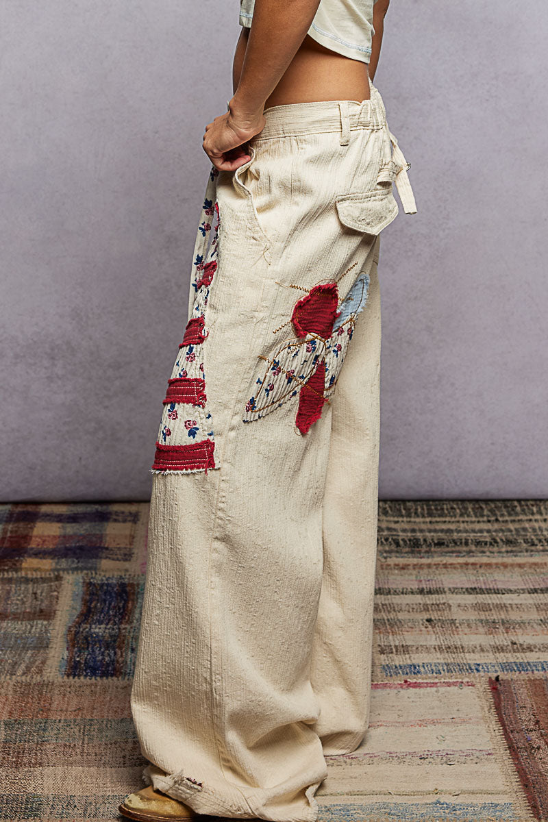 Person wearing beige pants with floral embroidery on a patterned rug.