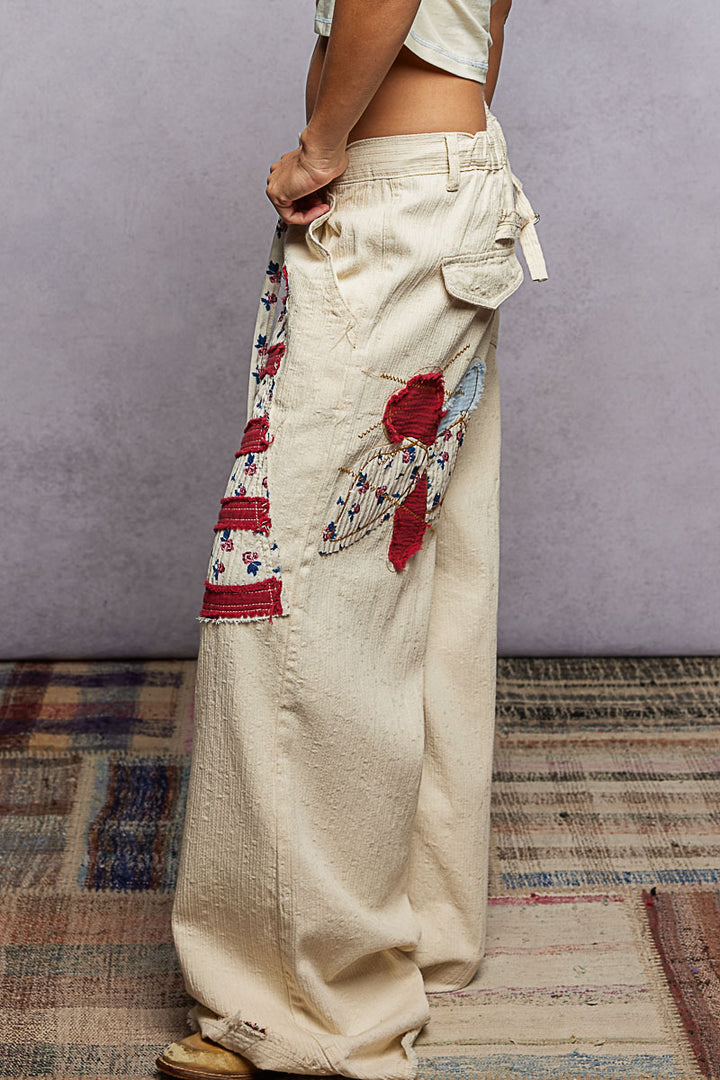 Person wearing beige pants with floral embroidery on a patterned rug.