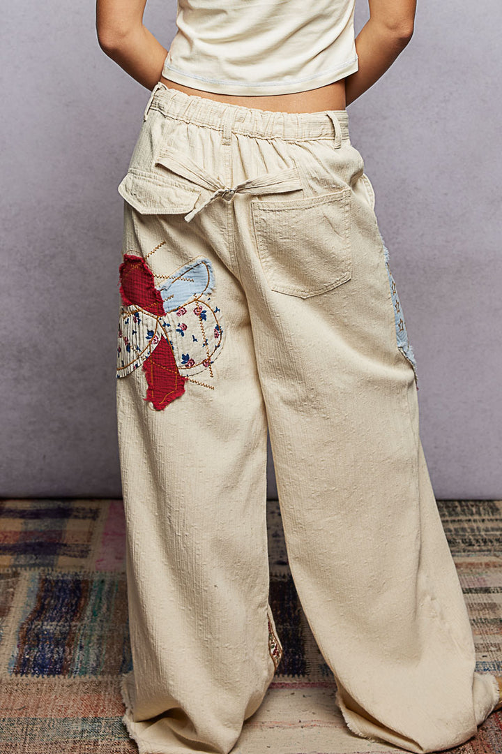 Beige wide-leg pants with colorful patches worn by a person against a plain background