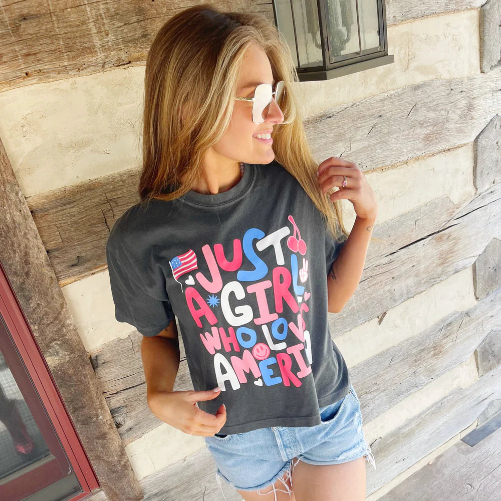 Woman wearing black graphic tee and denim shorts on wood background