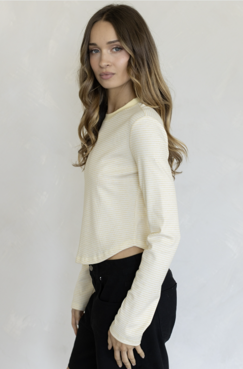 Woman wearing yellow long sleeve shirt and black pants on plain background