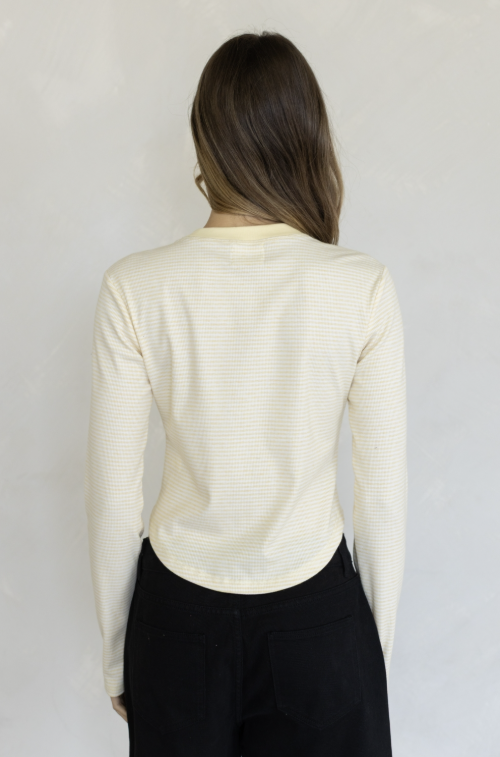 Woman shown from the back wearing yellow stripe long sleeve shirt and black pants on plain background