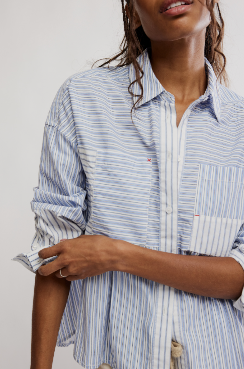 A close-up of a woman wearing a light blue and white vertically striped button-down shirt with rolled-up sleeves and a chest pocket.