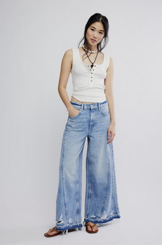 Woman wearing a white sleeveless top and light blue jeans on a plain background