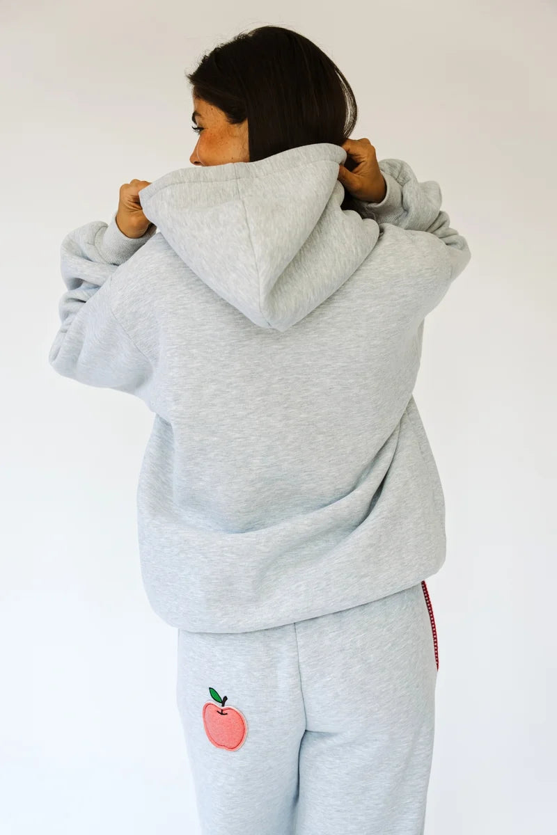 Woman shown from back with heather grey hoodie and sweatpants with apple applique on back on white background