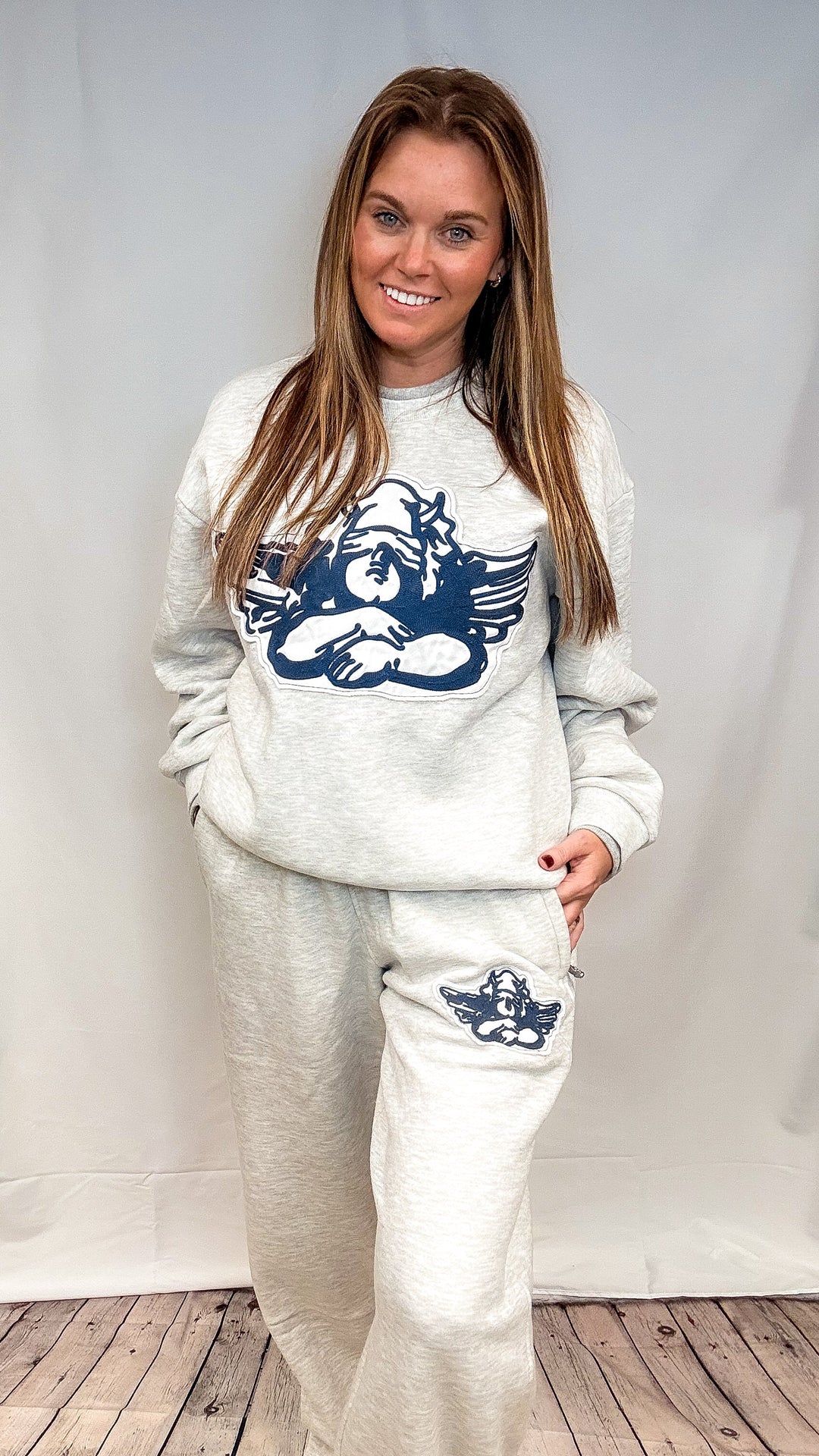 Woman wearing grey sweatsuit with cherub decal on white background