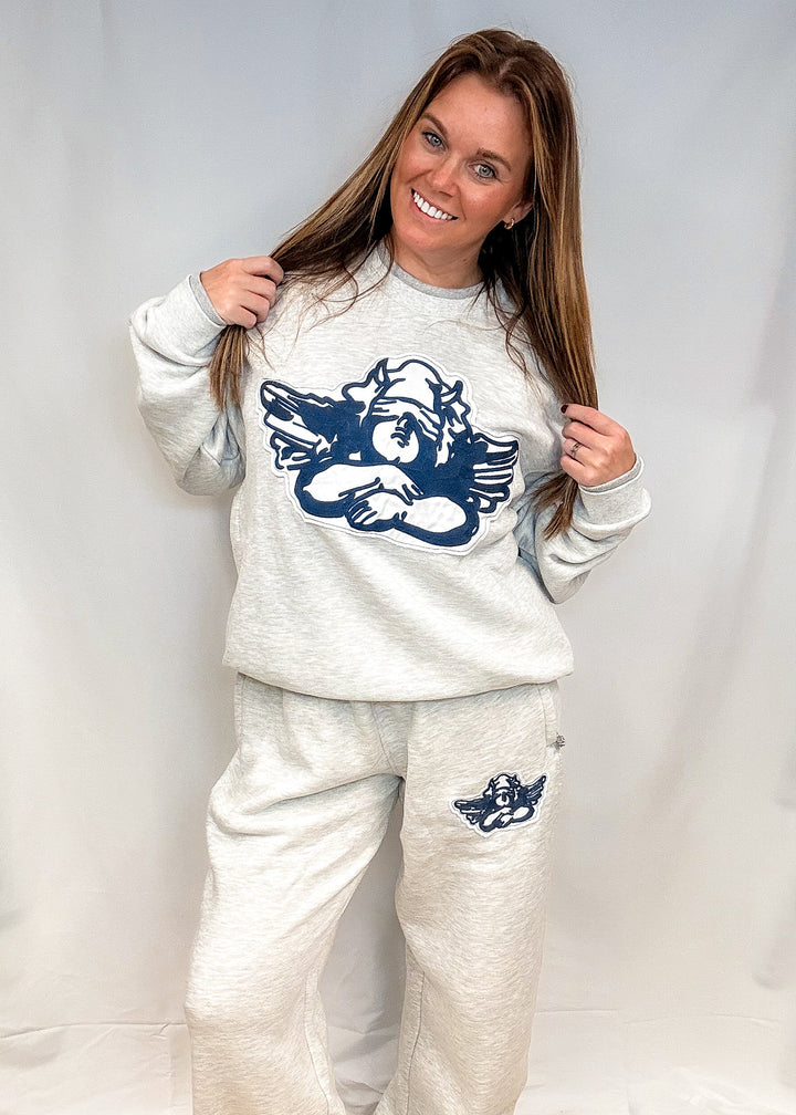 Woman wearing heather grey sweatsuit with cherub decal on front on white background