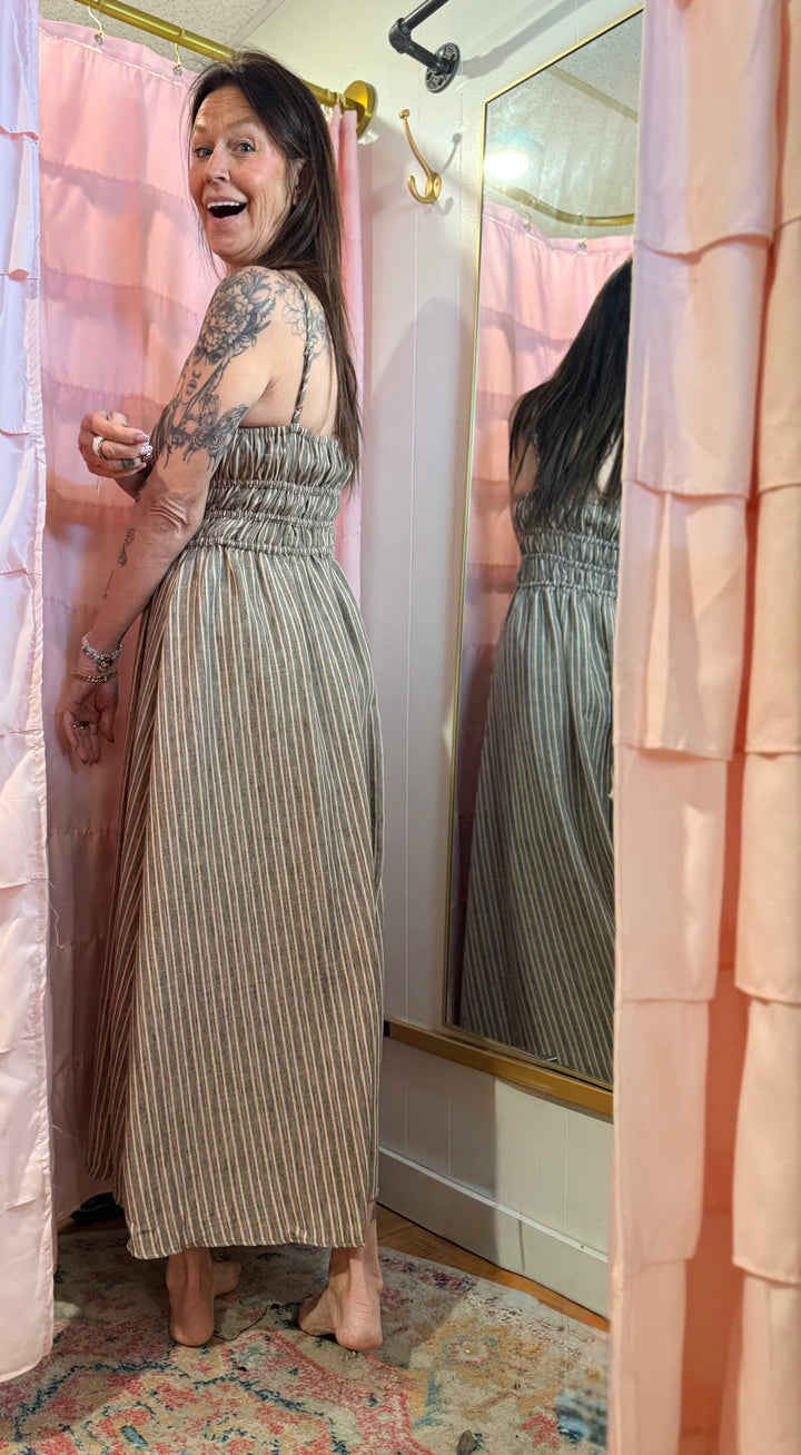 Woman in a striped dress standing in front of a mirror in a room with pink curtains.