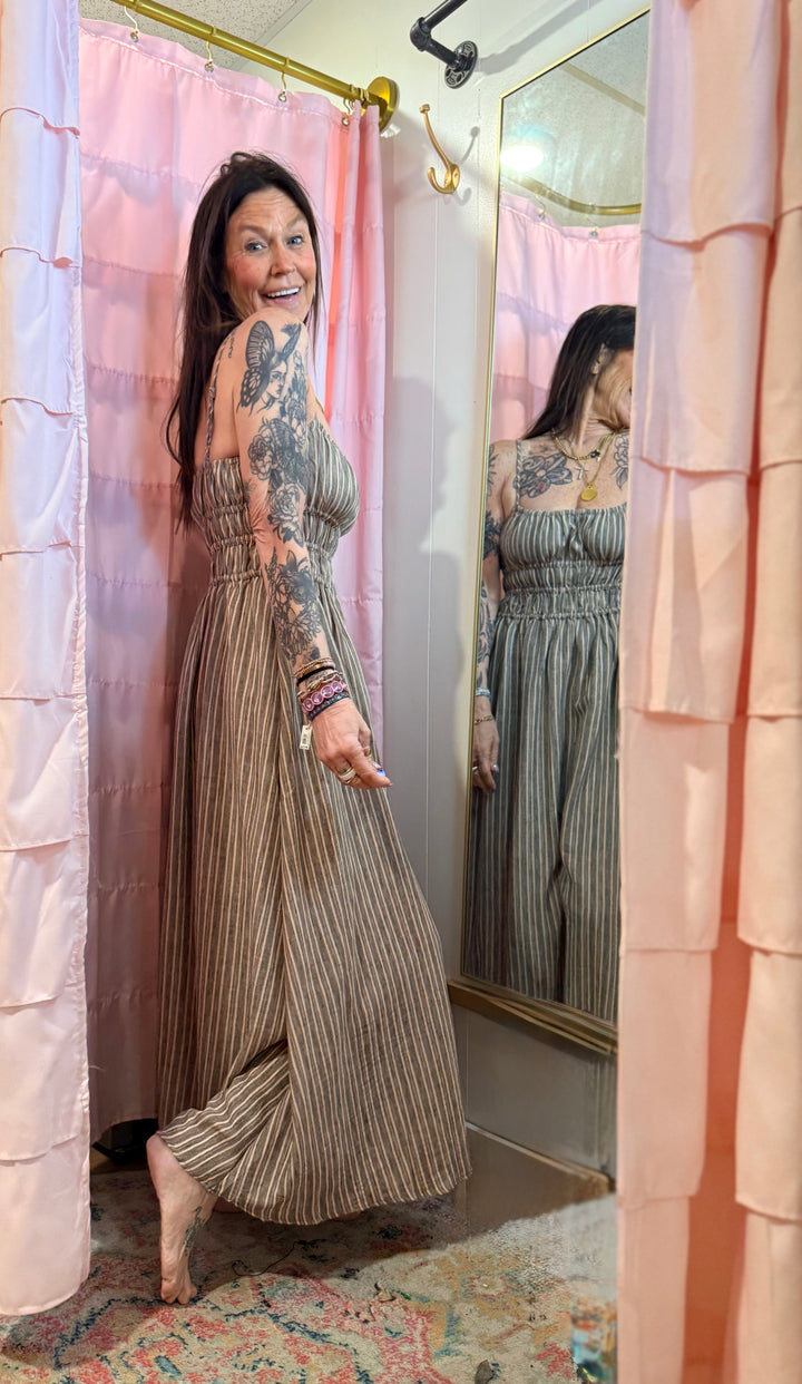 Woman in a patterned dress standing in front of a mirror with pink curtains.