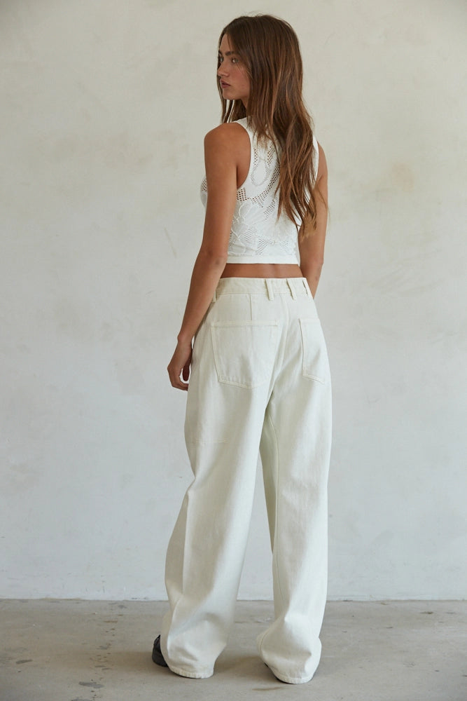 Woman wearing a white sleeveless top and wide-leg pants against a plain background