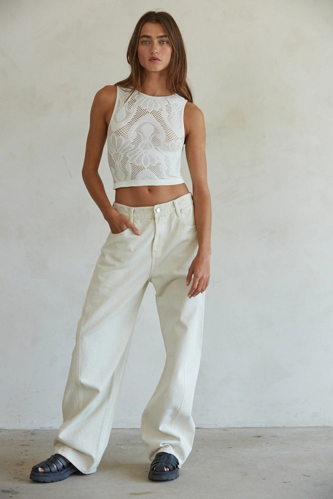 Woman wearing a white lace top and wide-leg pants against a plain background