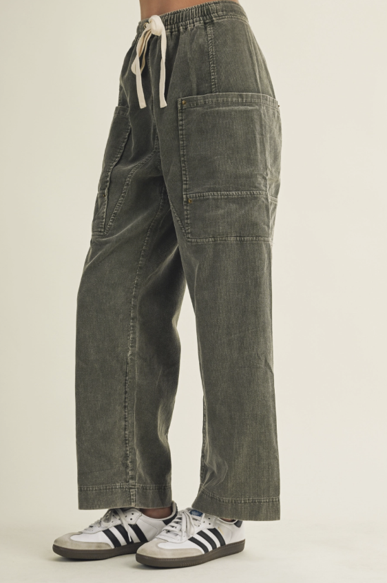 A person wearing wide-leg corduroy pants in an olive green color, paired with white sneakers featuring black stripes, shown from the waist down against a plain light background.
