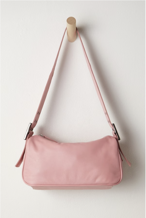 Pink handbag with a strap hanging on a wooden hook against a white wall.