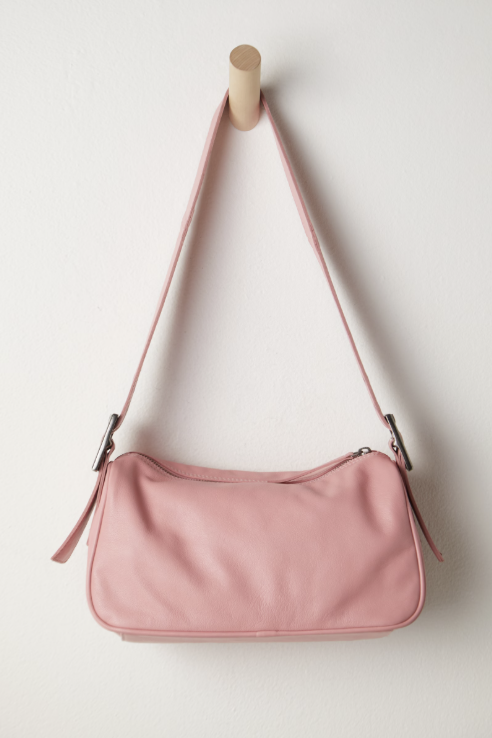 Pink shoulder bag hanging on a wooden hook against a white background