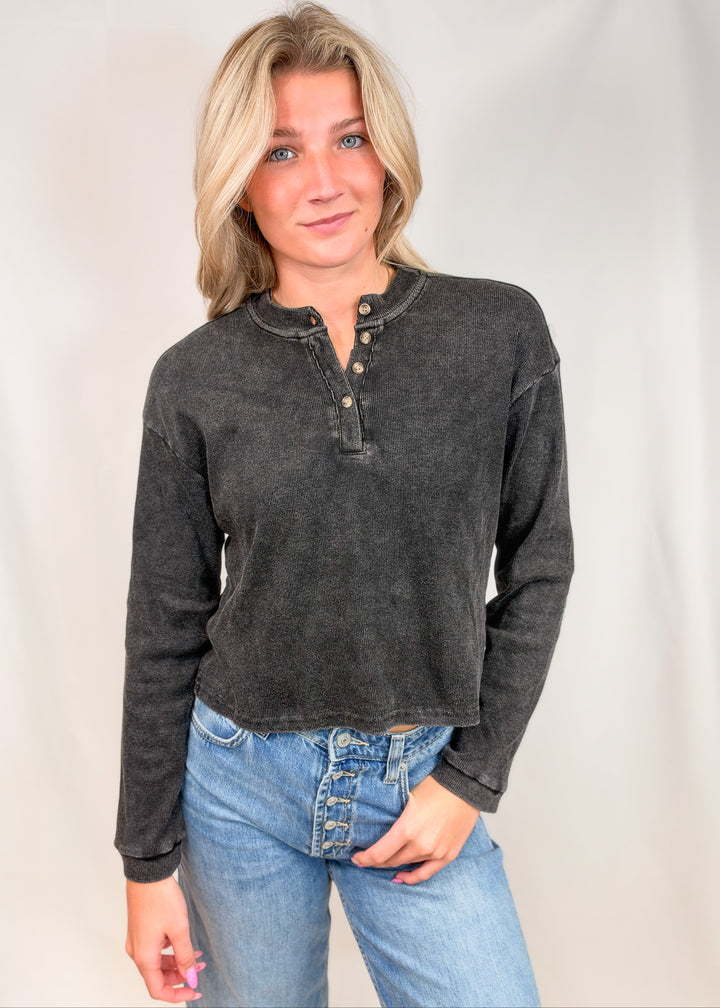 Woman wearing black ribbed henley top with jeans on plain background