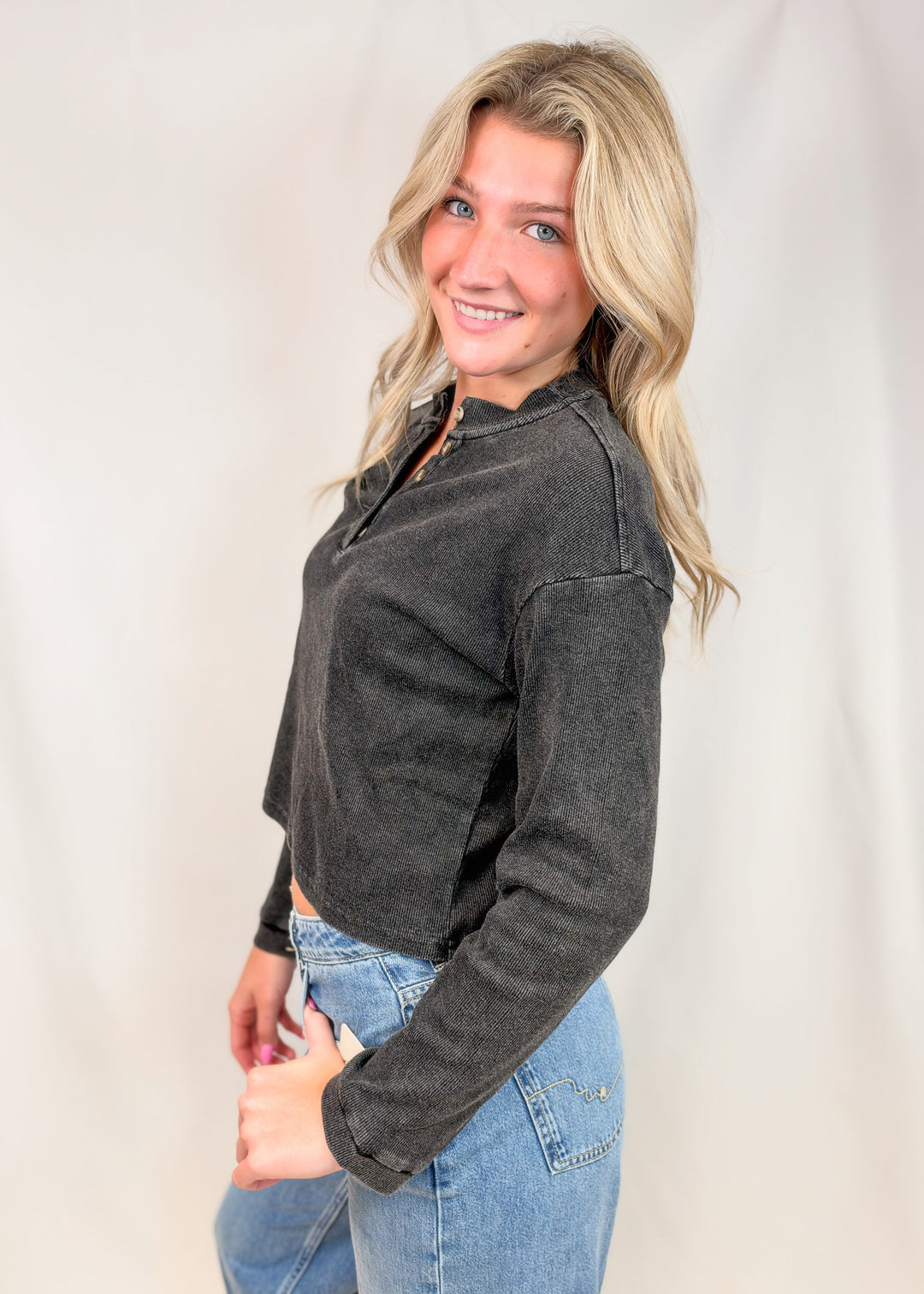 Woman shown from side view wearing black henley top and jeans on plain background