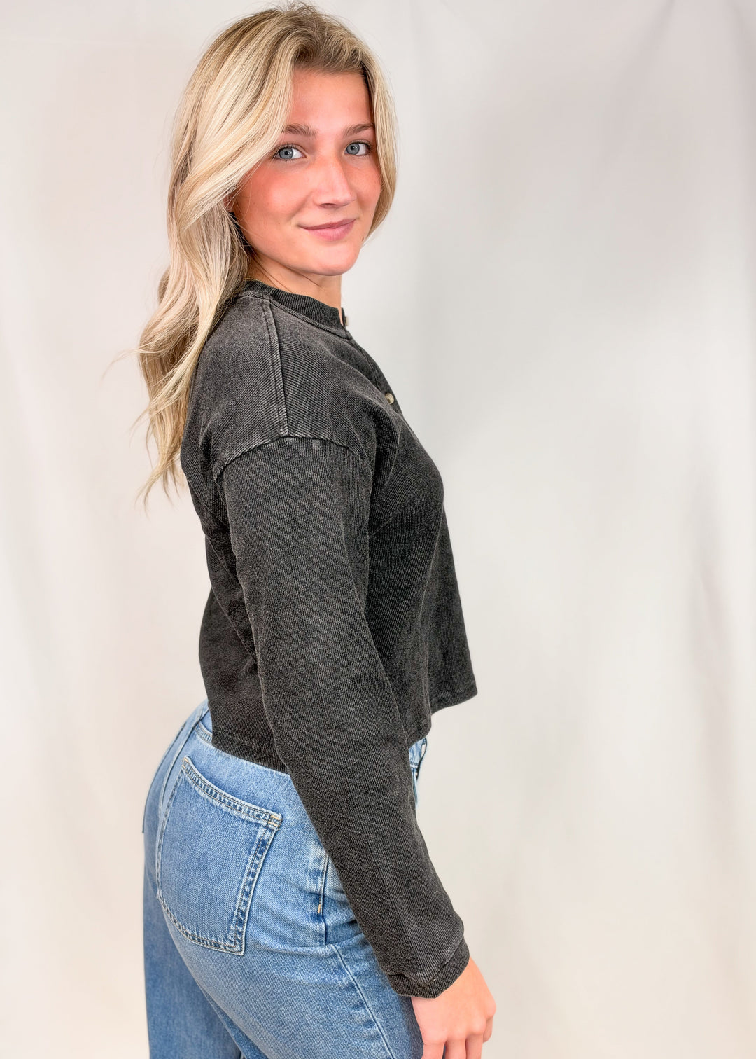 Woman shown from side view wearing black henley top with jeans on plain background