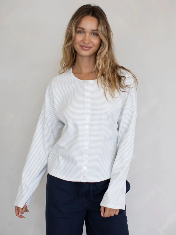 Woman wearing a white long-sleeve top with a subtle pattern against a plain background