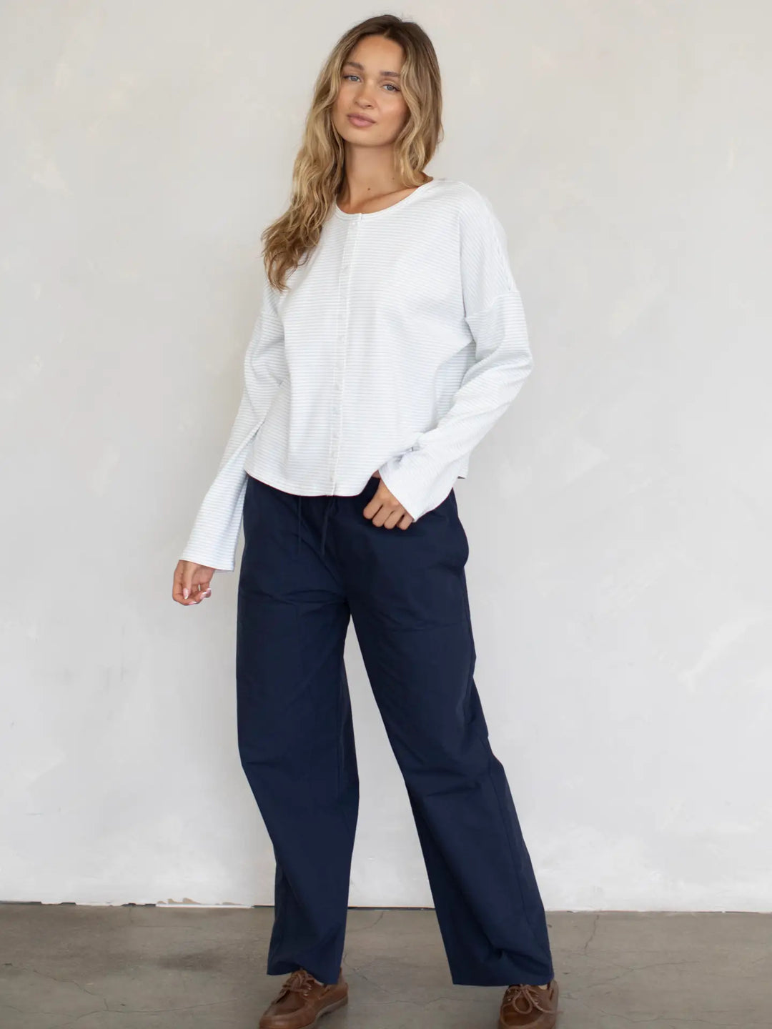 Woman wearing a white blouse and navy pants against a plain background