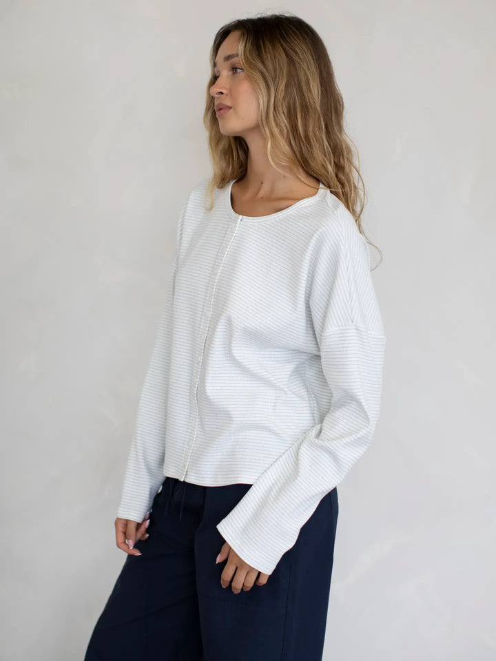 Woman wearing a white blouse and navy pants against a plain background