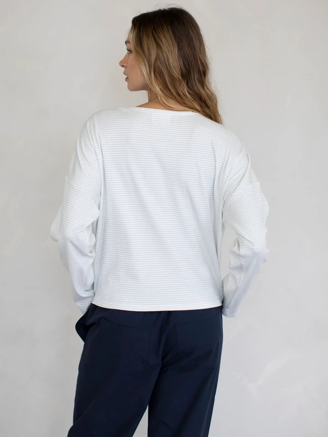 Person wearing a white textured top and navy pants against a plain background