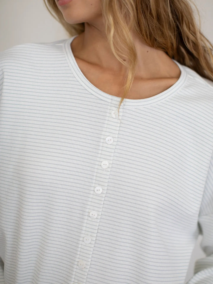 Close-up of a person wearing a light gray ribbed sweater with buttons.