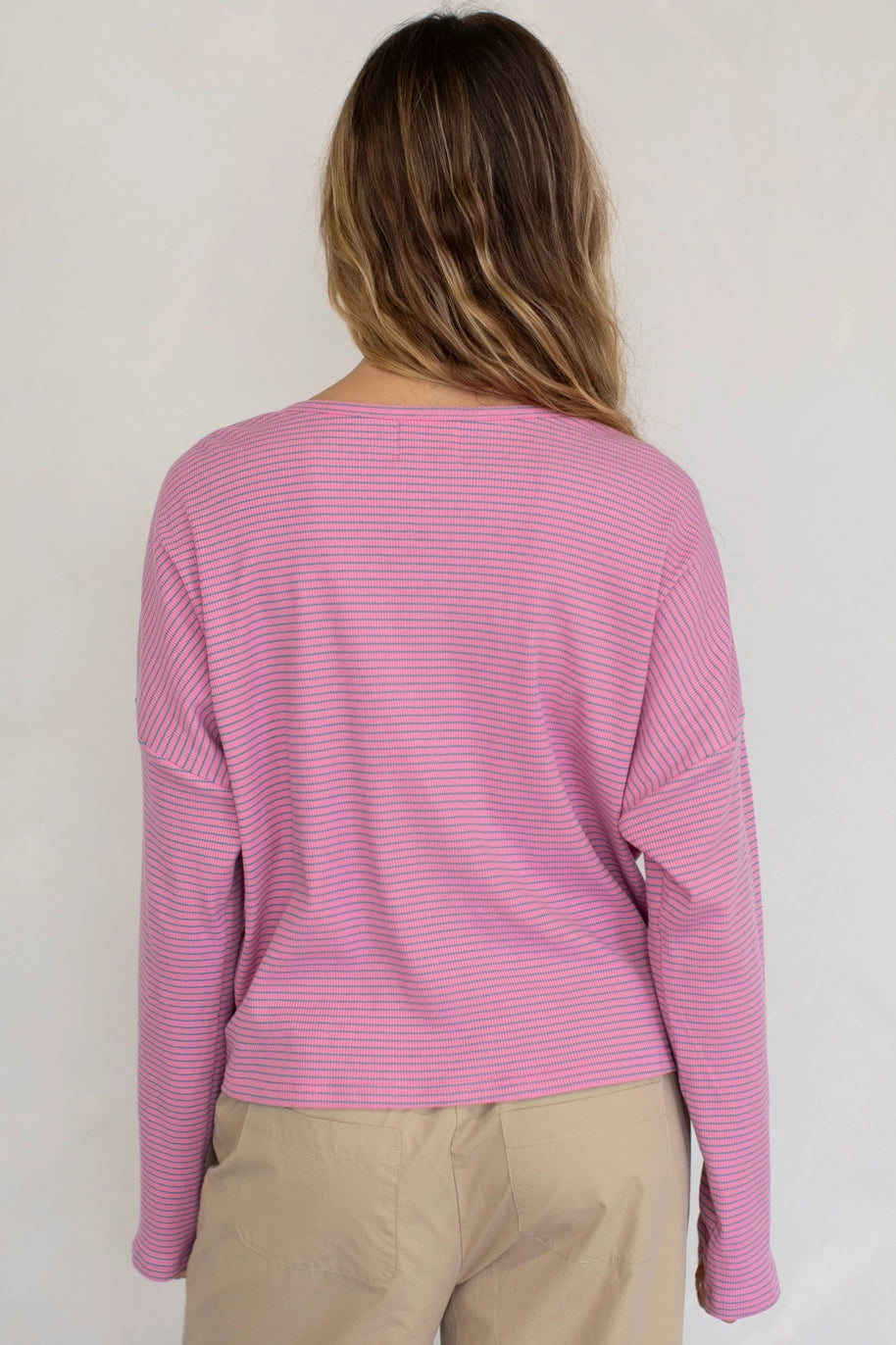 Person wearing a pink striped sweater and beige pants against a white background