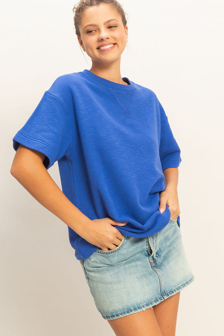 Woman wearing a blue oversized shirt and denim shorts on a plain background
