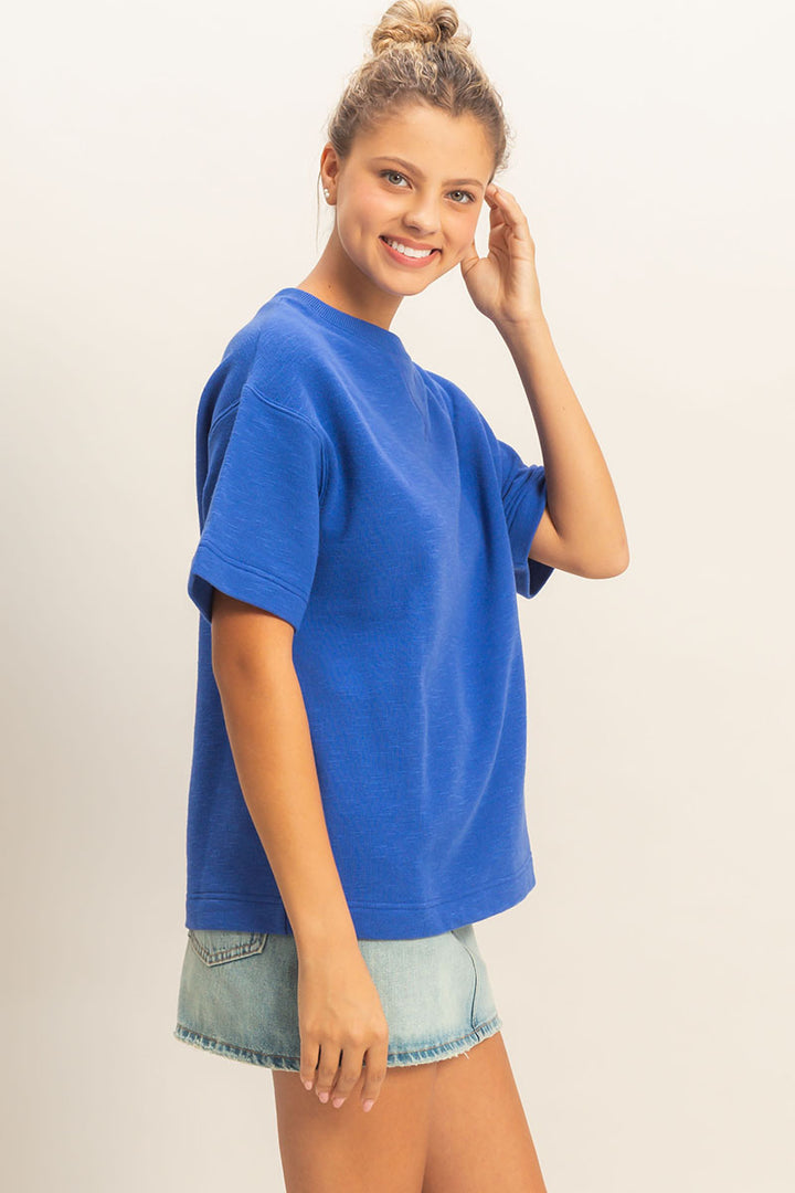 Woman wearing a blue oversized t-shirt and denim shorts on a plain background