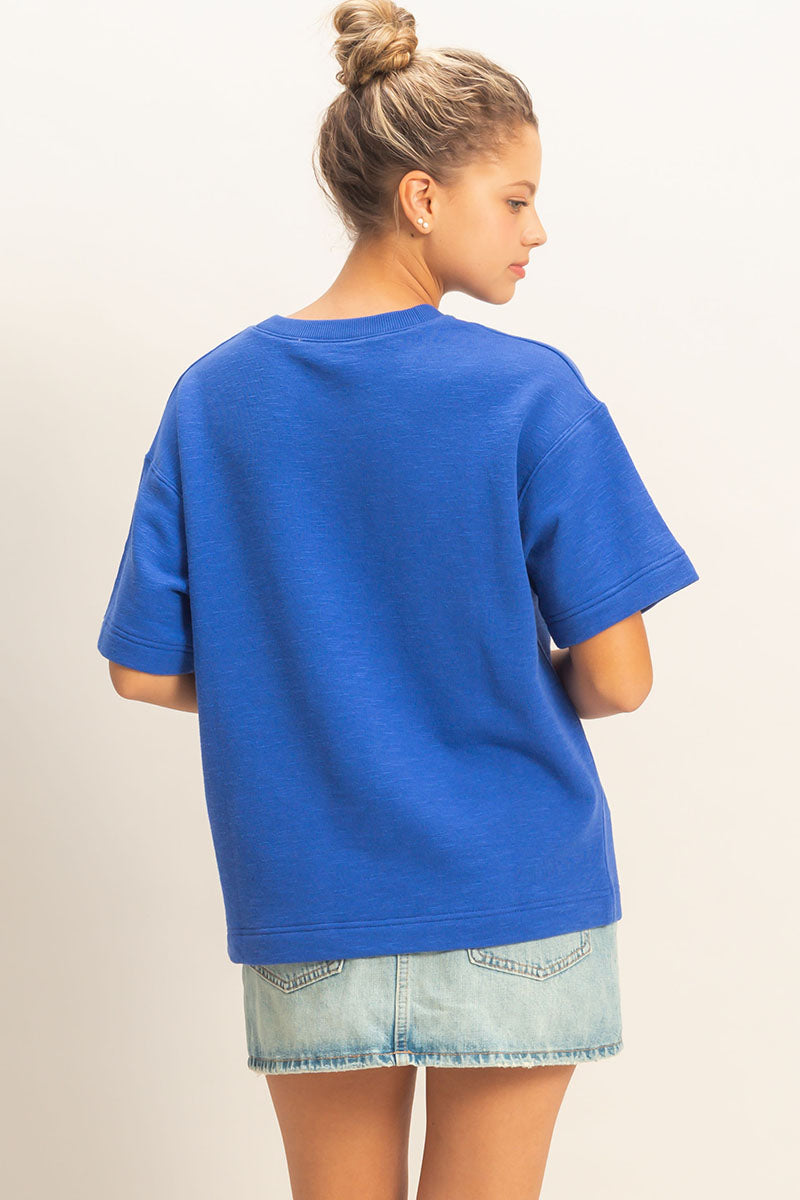Person wearing a blue oversized t-shirt and denim shorts on a plain background