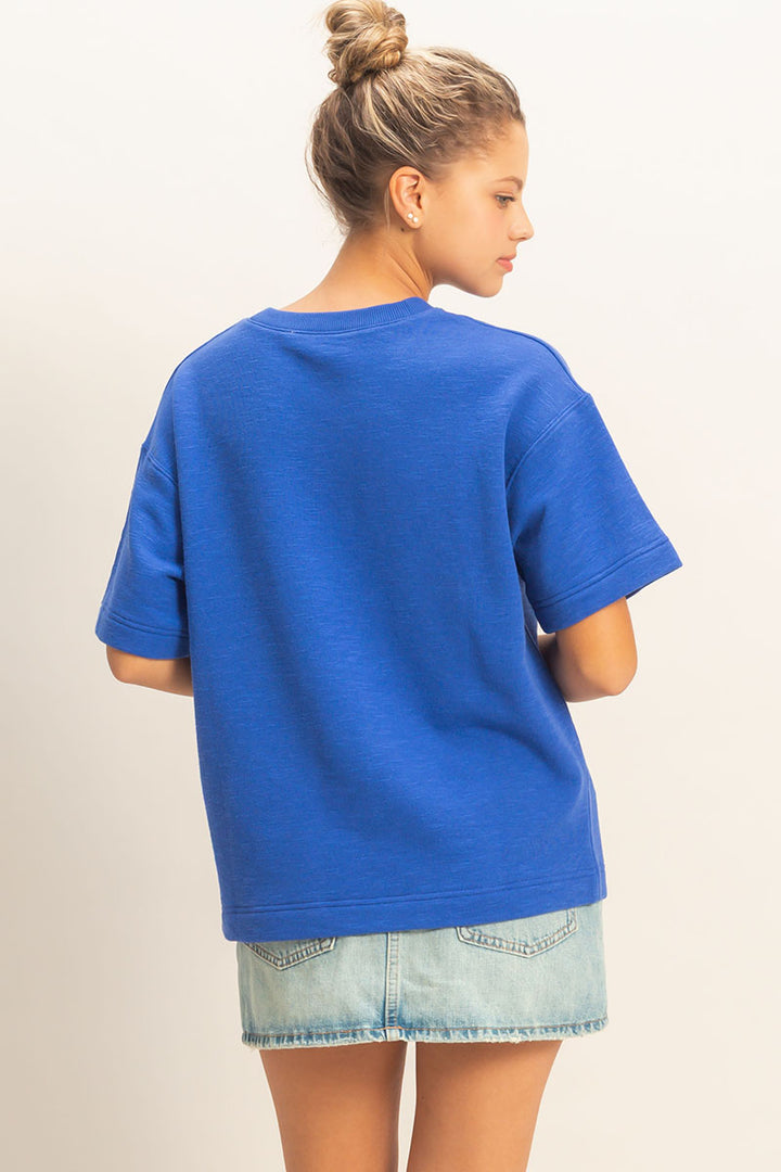 Person wearing a blue oversized t-shirt and denim shorts on a plain background
