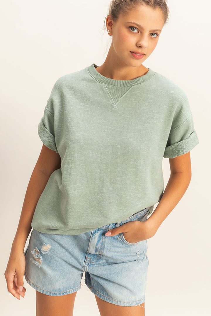 Person wearing a light green oversized sweatshirt and denim shorts on a plain background