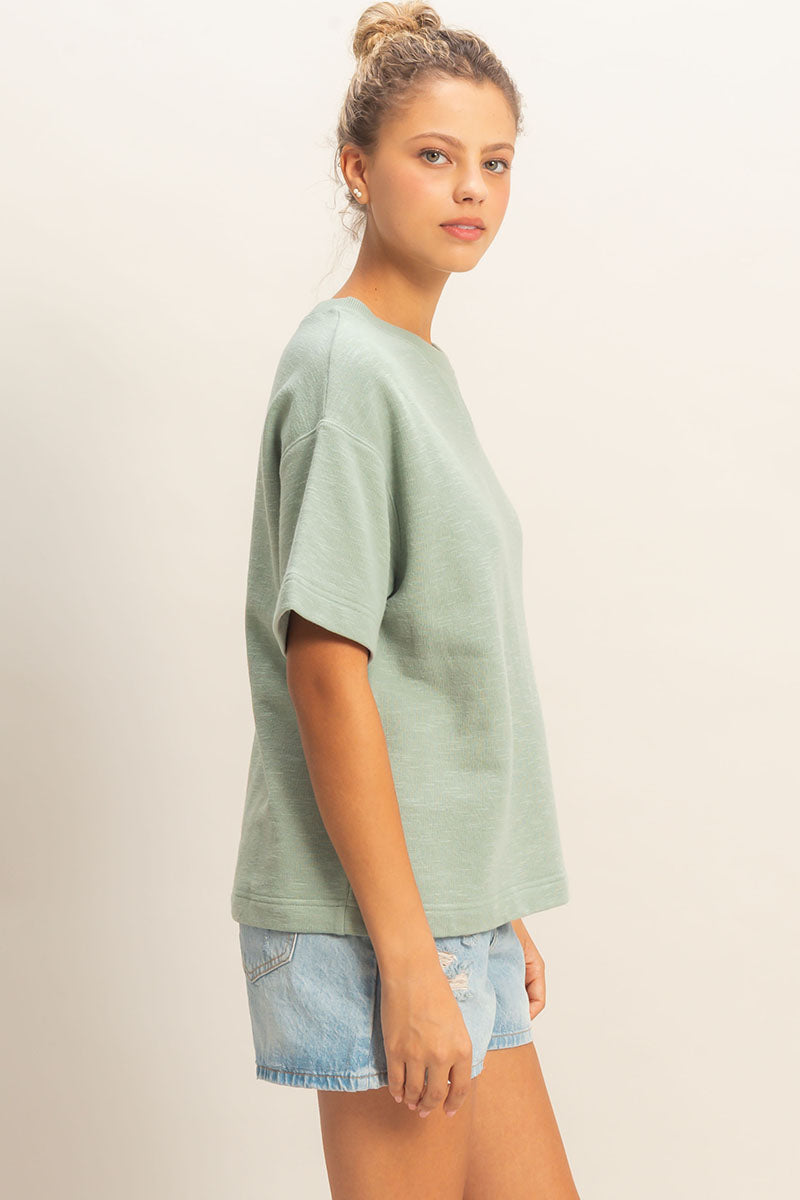 Woman wearing a light green t-shirt and denim shorts on a beige background