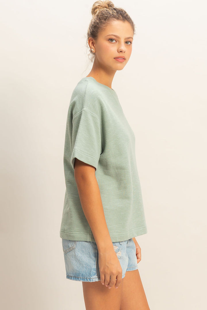 Woman wearing a light green t-shirt and denim shorts on a beige background