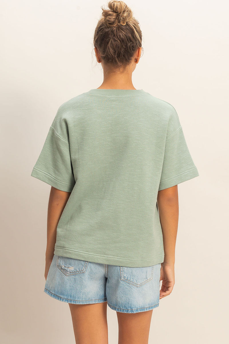 Person wearing a light green t-shirt and denim shorts on a plain background