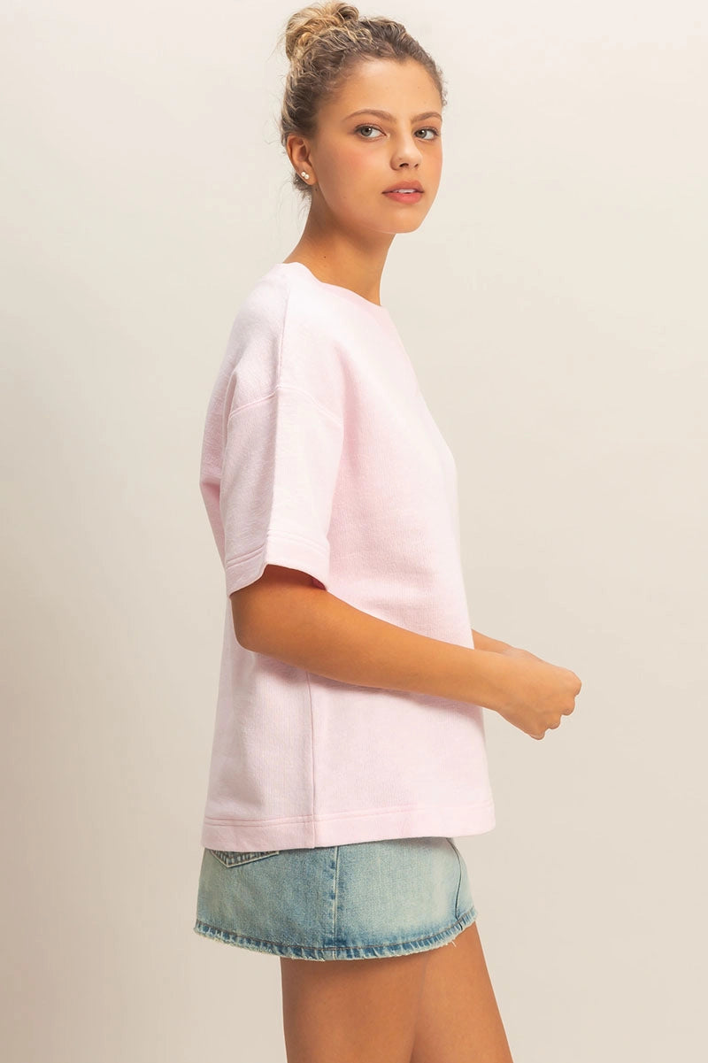 Woman wearing a light pink oversized t-shirt and denim shorts on a plain background
