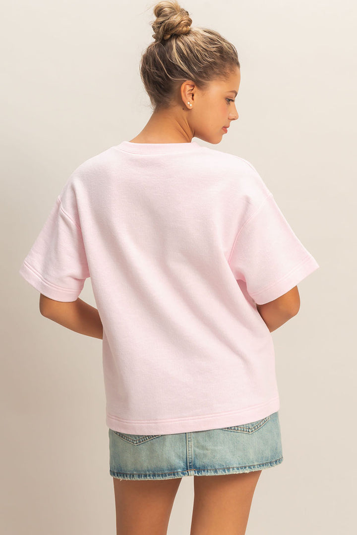 Person wearing a light pink oversized t-shirt and denim shorts on a plain background